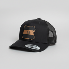 Black trucker cap with brown leather patch on a light gray background