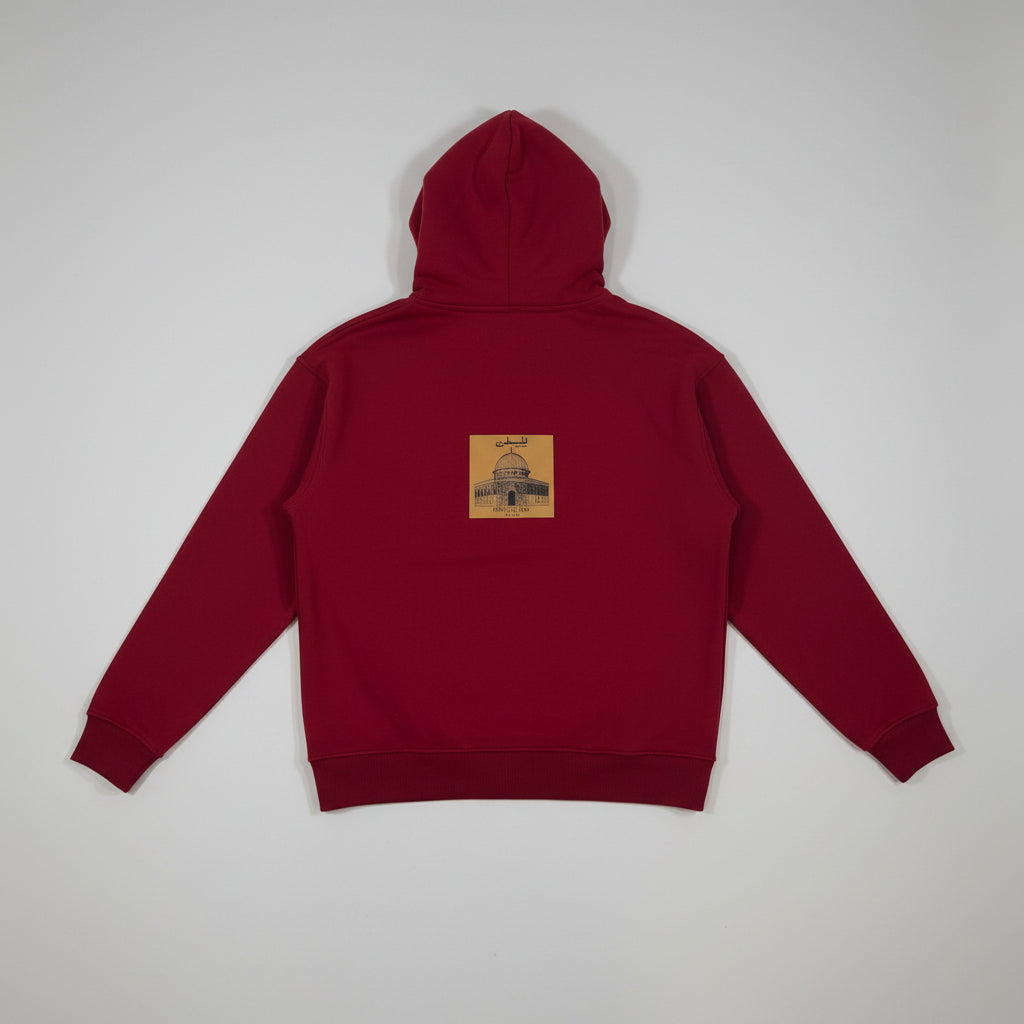 A dark red pullover hoodie shown from the back, featuring a small square graphic patch centered on the upper back with a building illustration and the text 'The Art of.